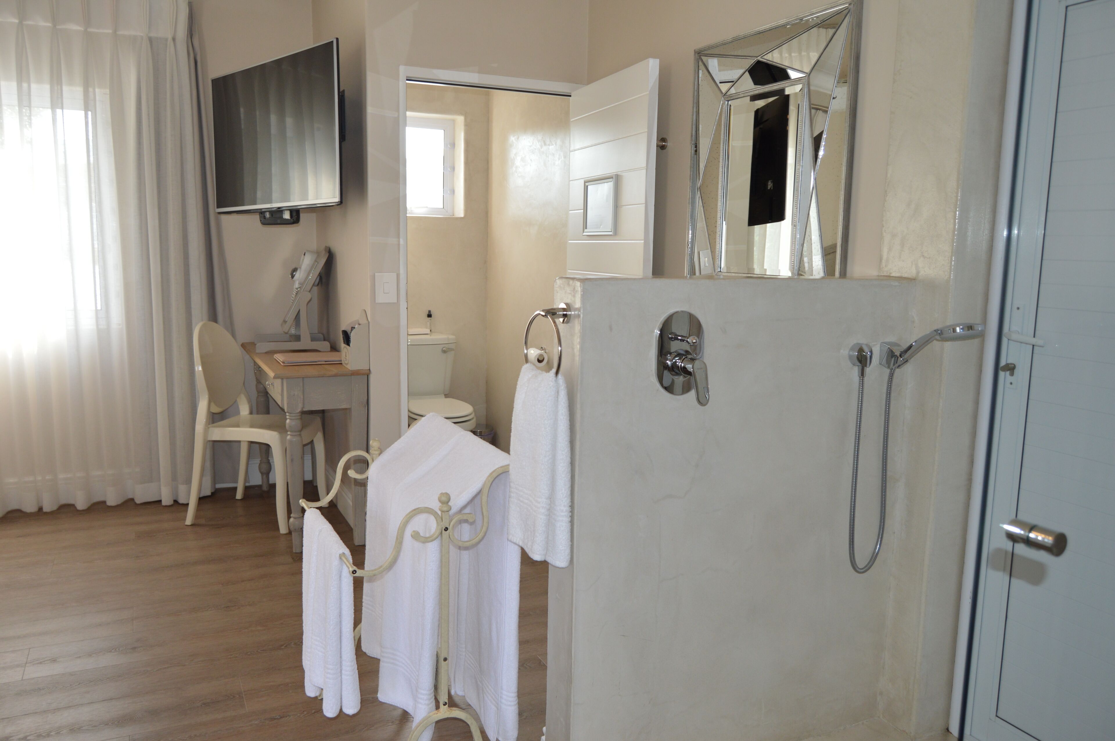 A bathroom with a shower, toilet, and sink. There is a chair and a towel rack with towels.