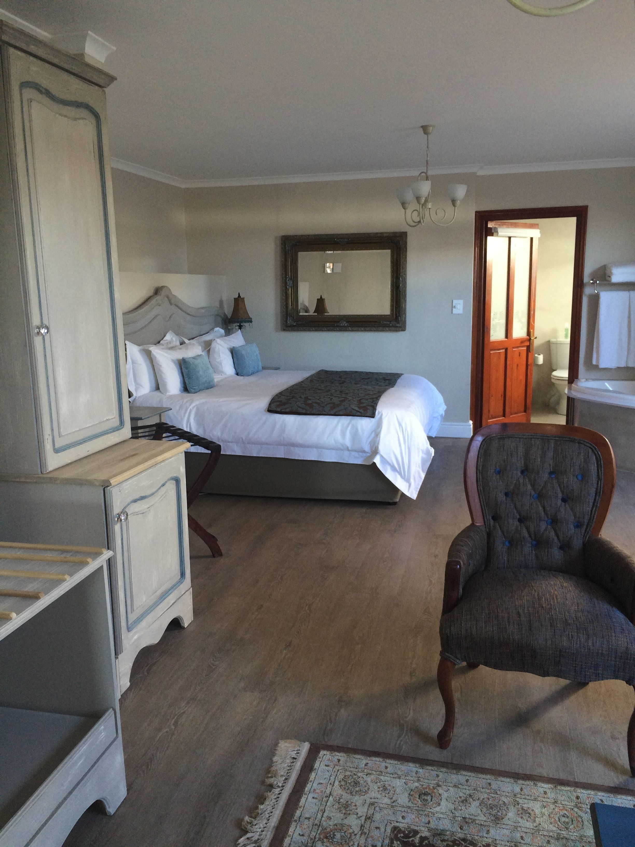 A bedroom with a bed, a chair, a dresser, and a mirror.
