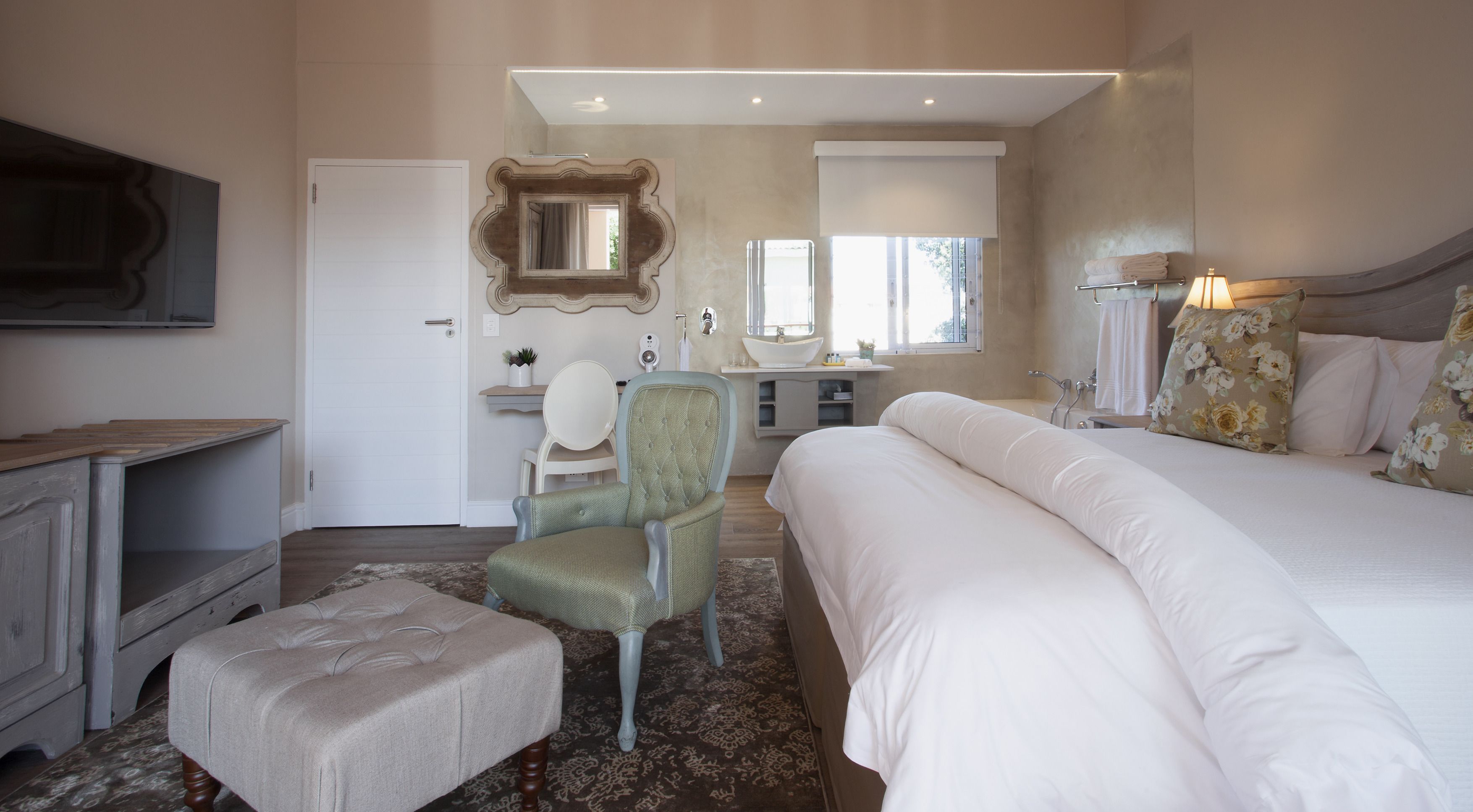 A bedroom with a large bed, a chair, a dresser, a vanity with a mirror, and a window.