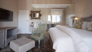 A bedroom with a large bed, a chair, a dresser, a vanity with a mirror, and a window.