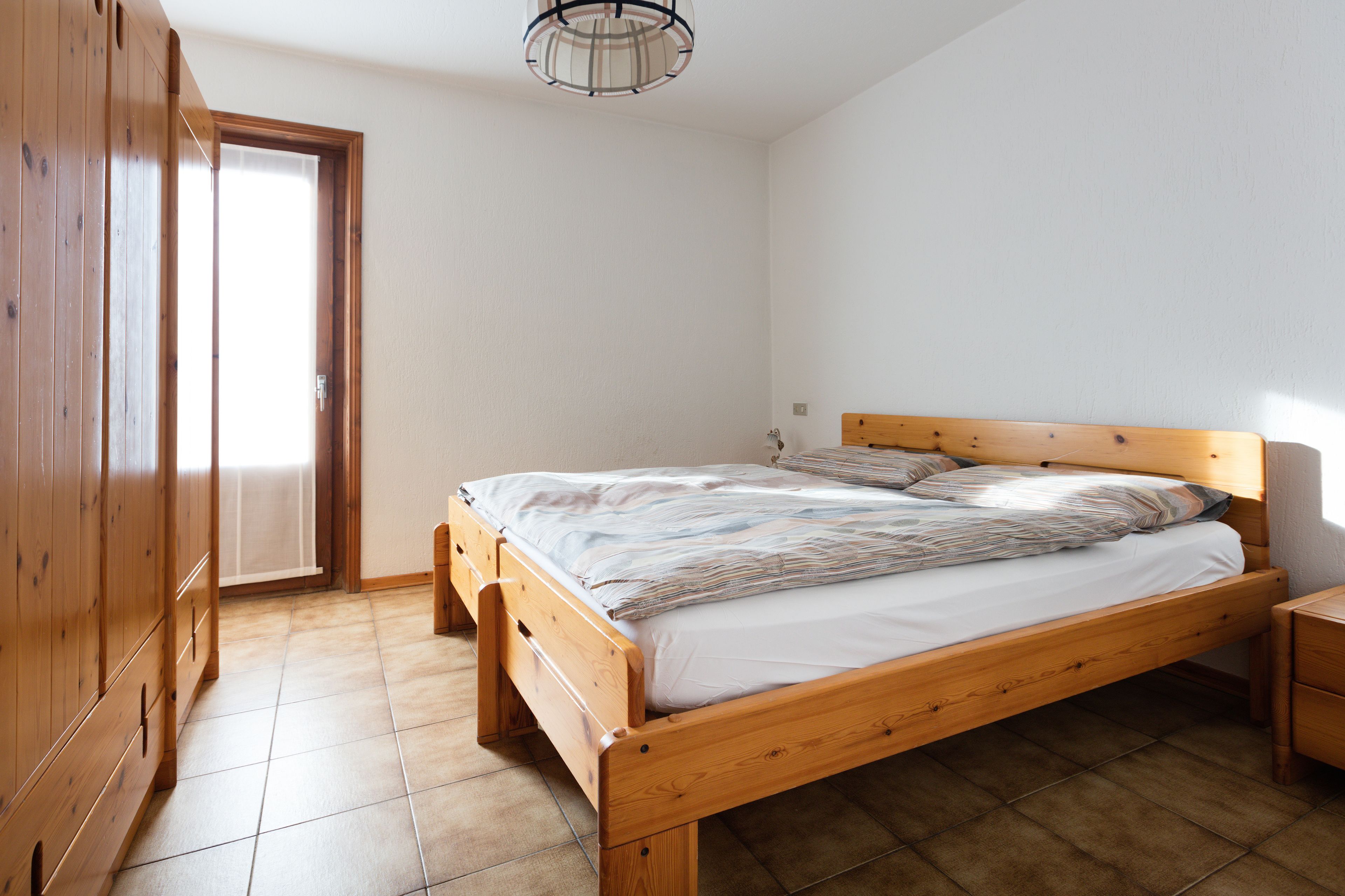 A bedroom with a wooden bed, a wooden wardrobe, and a tiled floor.
