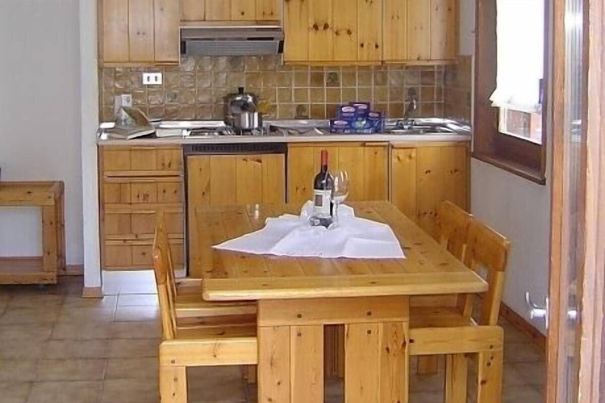 A kitchen with wooden cabinets, a tiled backsplash, and a dining table set with a wine bottle and glasses.