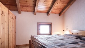 A bedroom with a wooden ceiling, a window, a bed with a patterned bedspread, and a bedside lamp. - Residence Gardenia (Livigno)