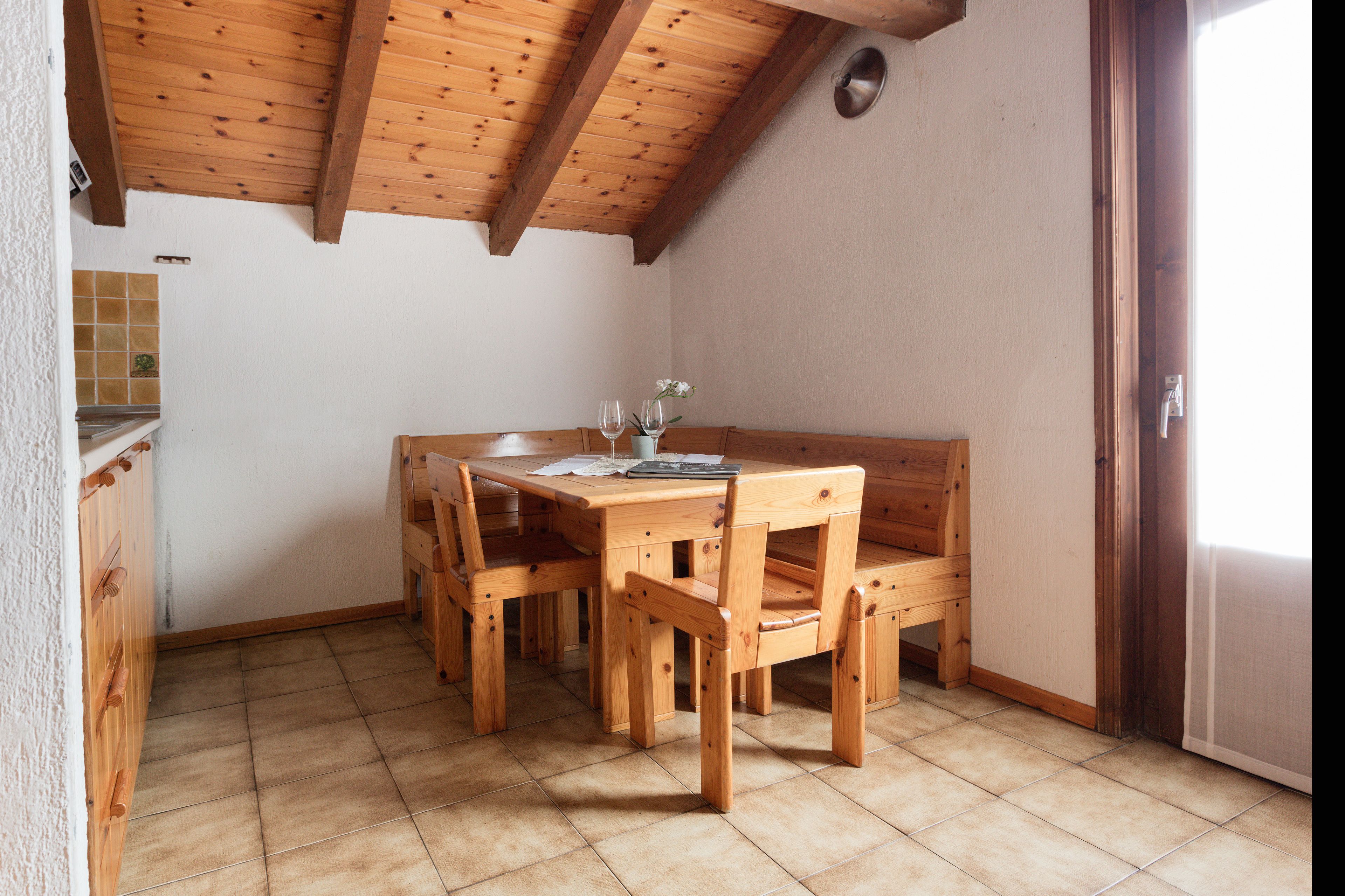 A wooden dining table with chairs, a bench, and a small vase with flowers.
