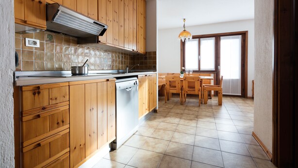 A kitchen with wooden cabinets, a dishwasher, and a dining area with a table and chairs. - Residence Gardenia (Livigno)