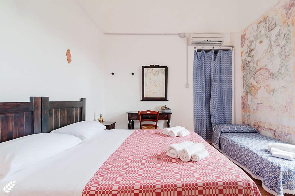 Quarto de hotel com uma cama grande, uma cama menor, uma escrivaninha e área de chuveiro.