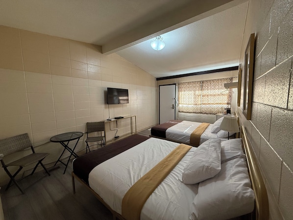 Quarto de hotel com duas camas, televisão, escrivaninha e cadeira.