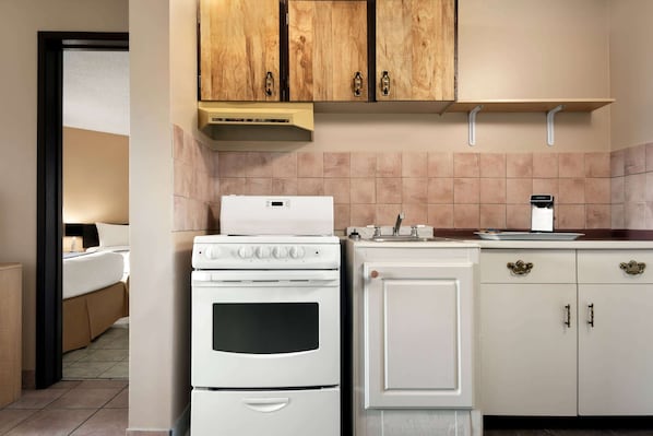 A compact kitchen with a white stove, oven, and a small sink. There are wooden cabinets above the countertop and a beige backsplash. - Thriftlodge Edmonton (Edmonton)