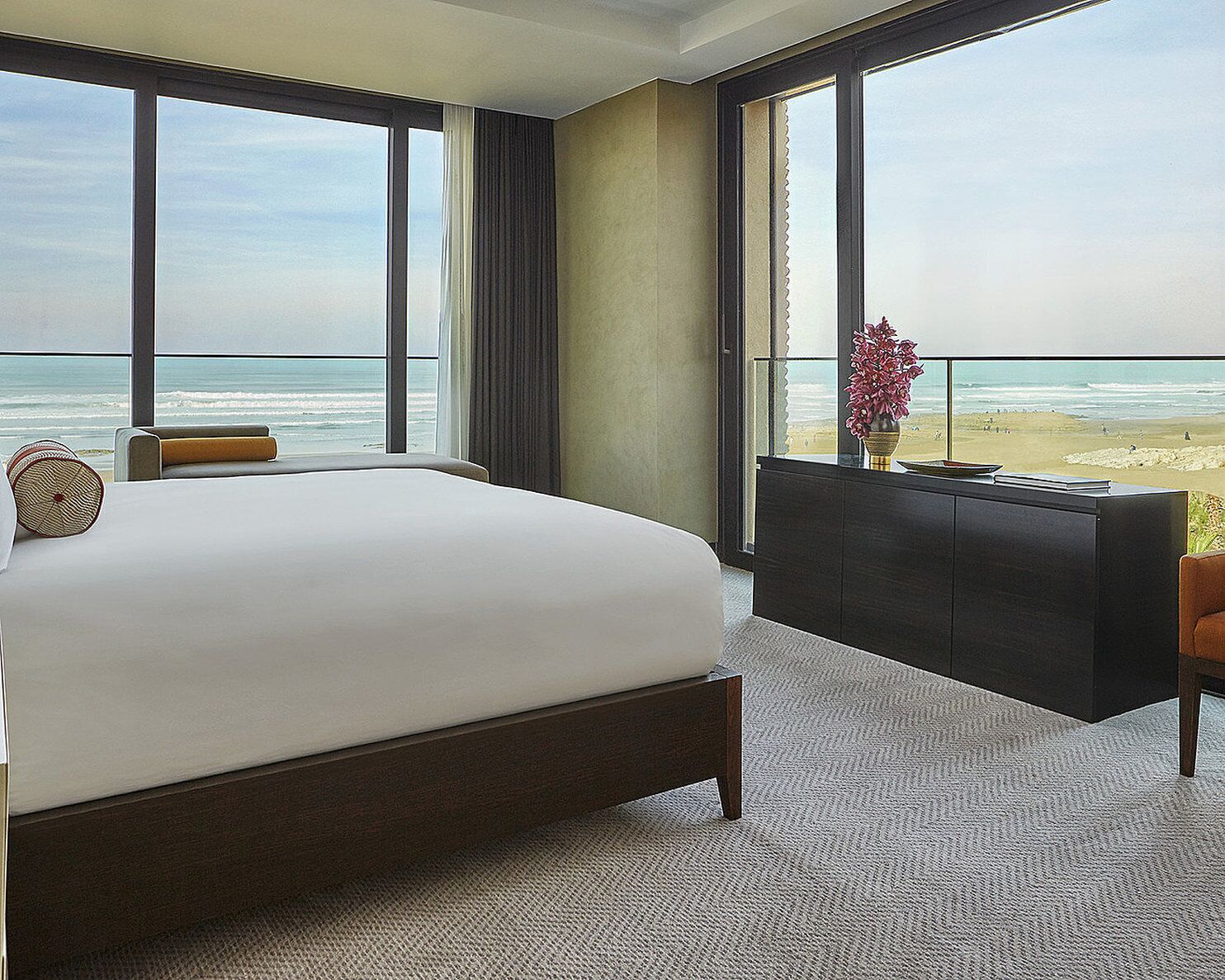 A hotel room with a large bed, a desk, and a view of the beach.