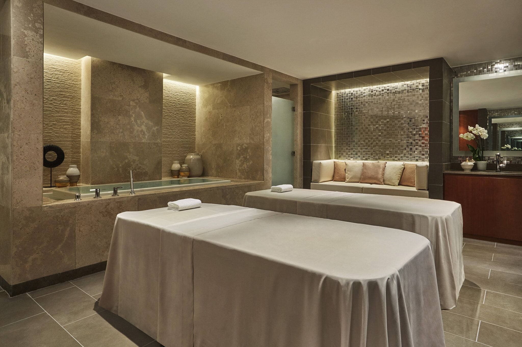 A spa area with two massage tables, a large mirror, and a seating area with cushions.