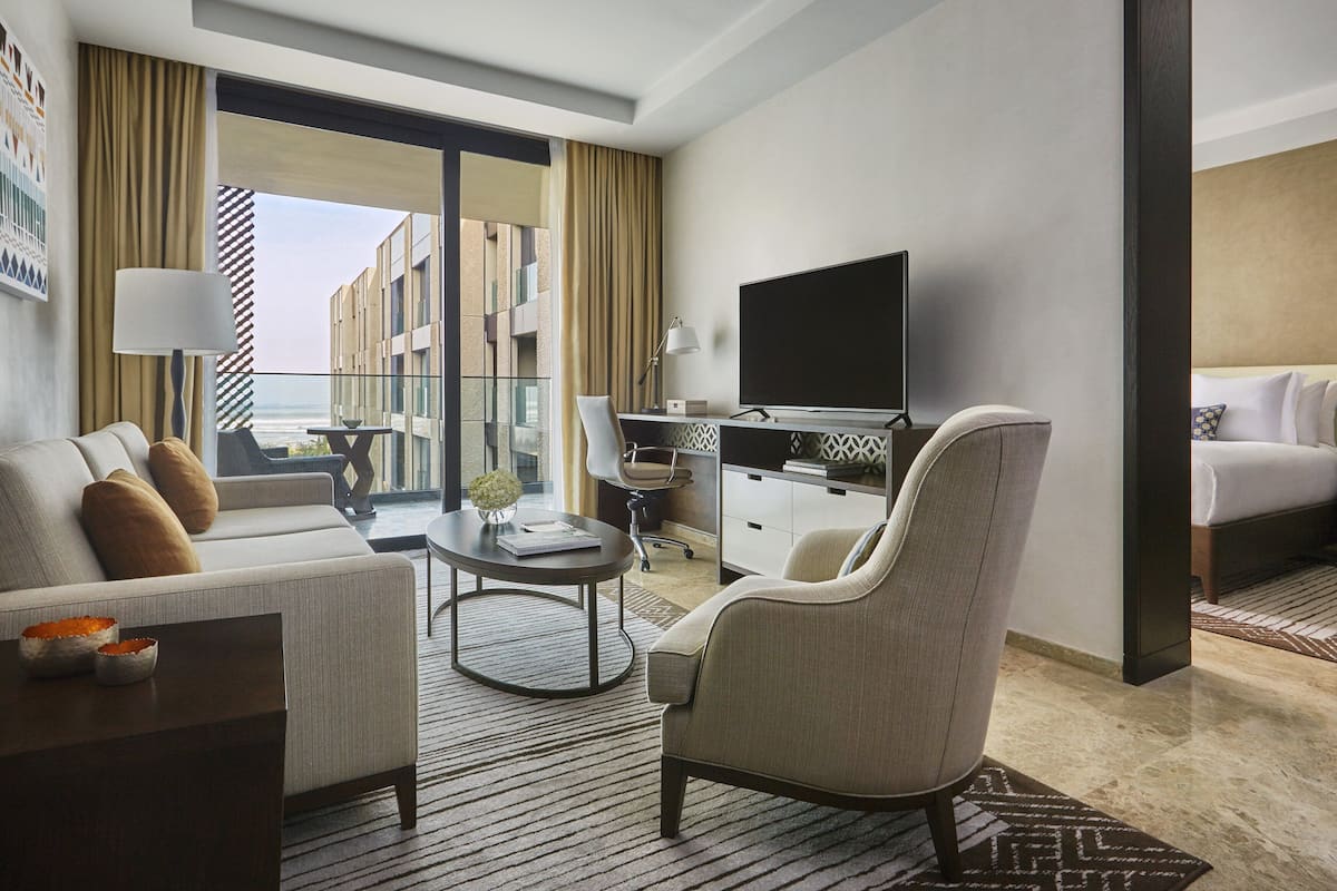 A modern hotel room with a sofa, a desk with a flat-screen TV, a chair, and a bed.