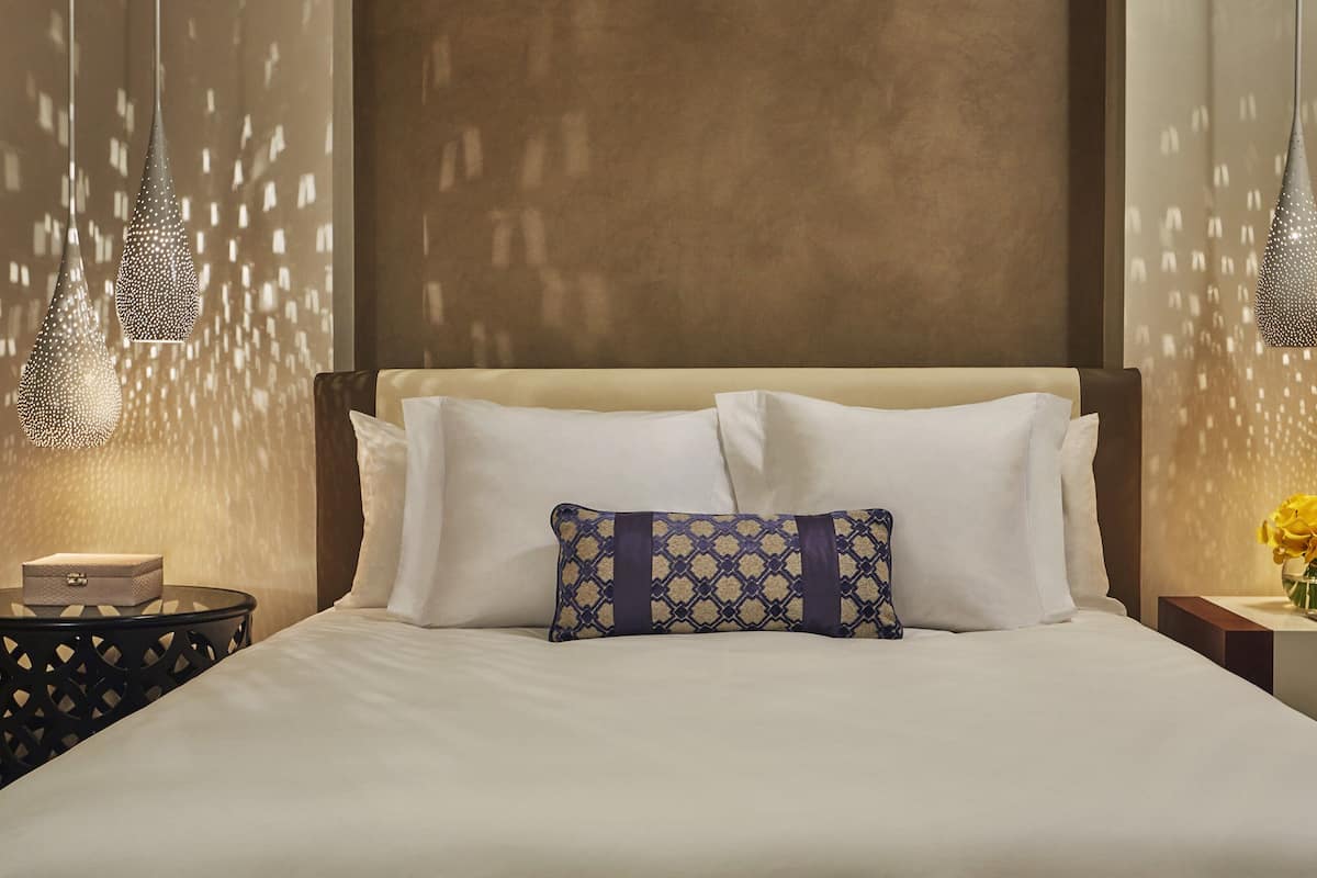 A neatly made bed with white linens and a patterned pillow, flanked by two bedside tables with lamps.
