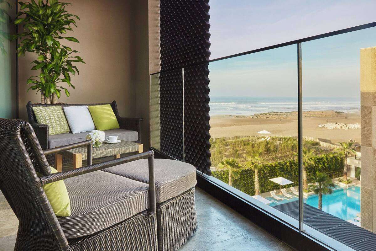 A balcony with wicker furniture, a potted plant, and a view of the beach and pool.
