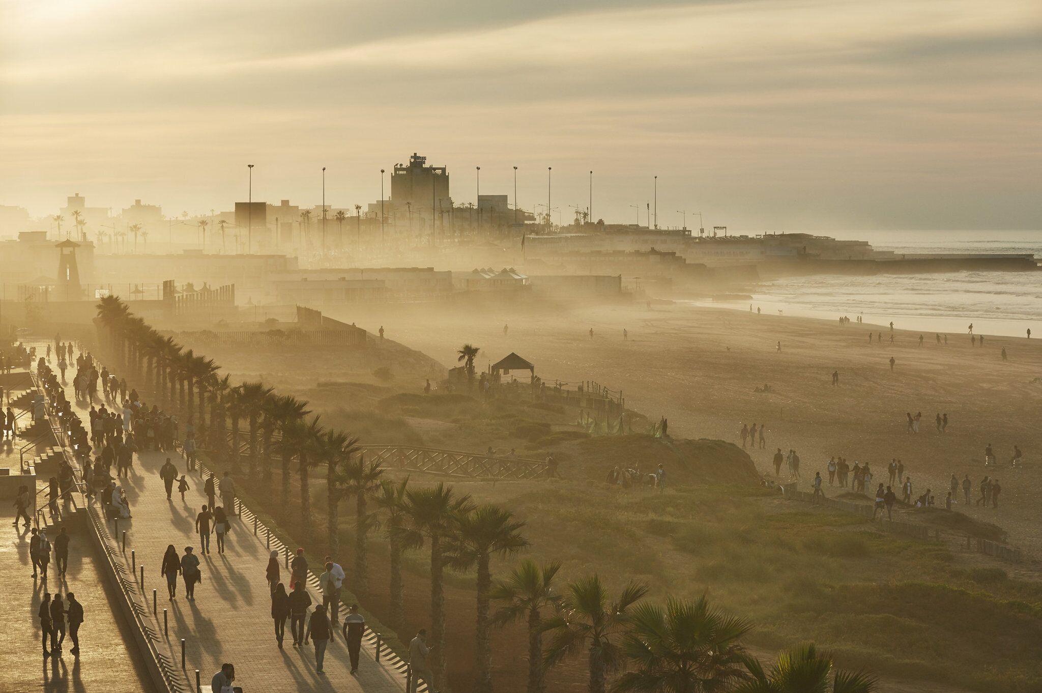 Eine Uferpromenade mit langer Fußgängerzone, Palmen und Blick auf Strand und Meer.