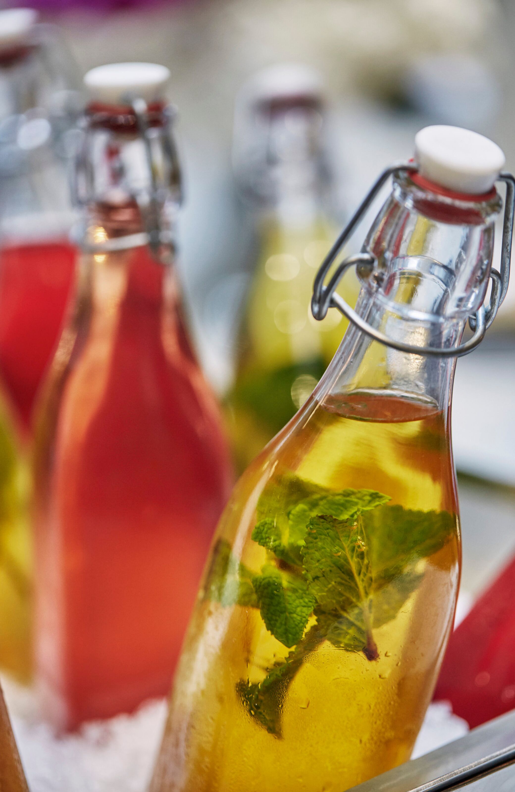 A close-up of three glass bottles with metal caps, each containing a different colored liquid and mint leaves.