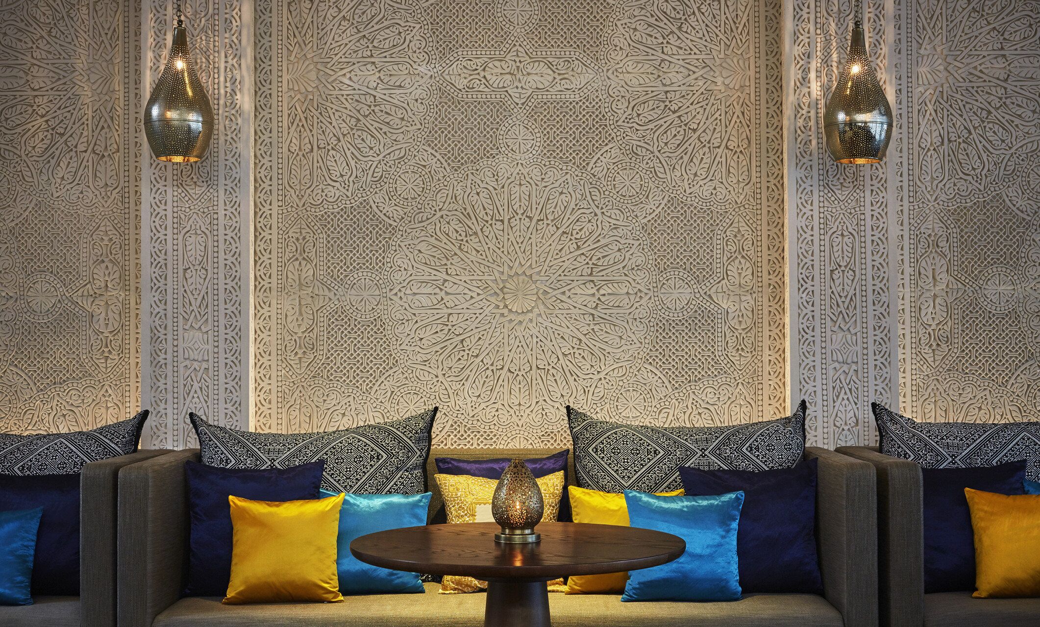 A room with a patterned wall, a sofa with cushions, and two hanging lamps.
