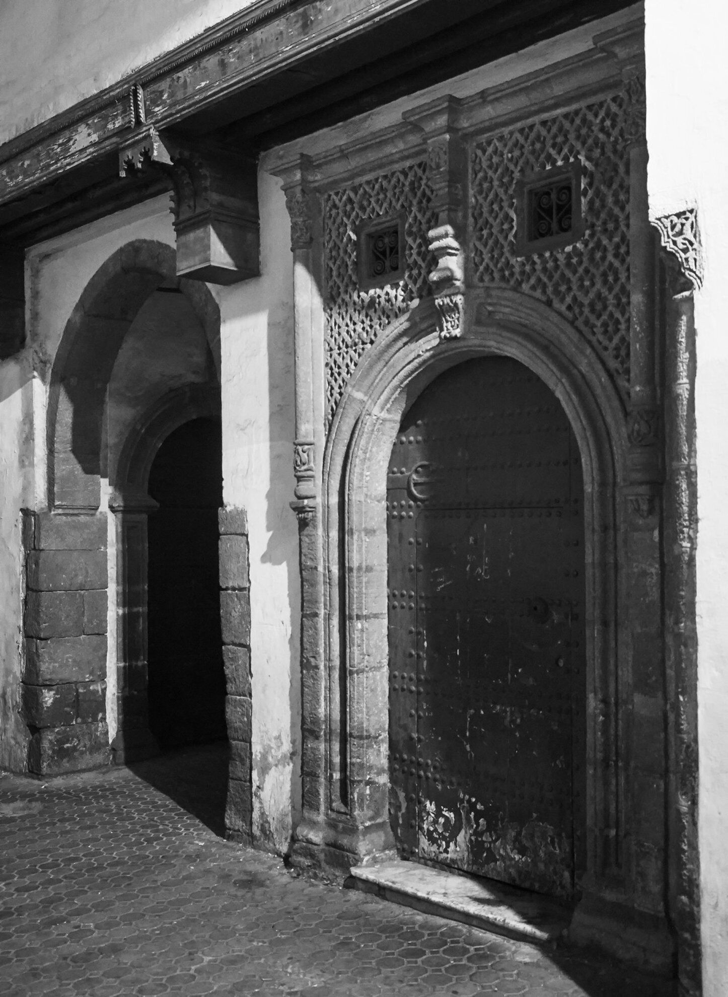 Un arco con elaborada labor de piedra y una puerta grande y oscura.