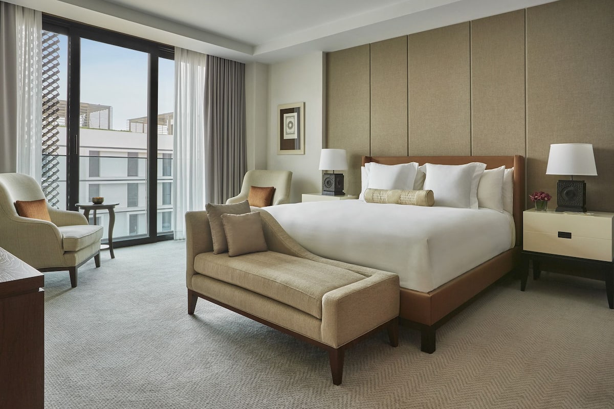 A hotel room with a large bed, two armchairs, a small table, and a nightstand with lamps.