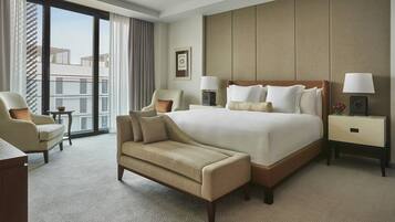 Una habitación de hotel con una cama grande, dos sillones, una mesita pequeña y una mesita de noche con lámparas.