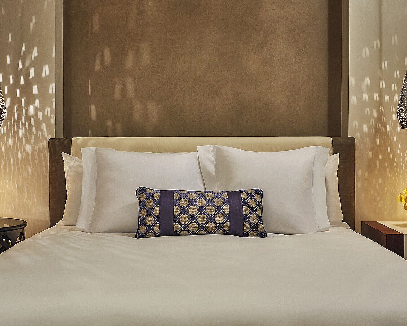 Una cama bien hecha con sábanas blancas y un cojín decorativo con estampado geométrico.