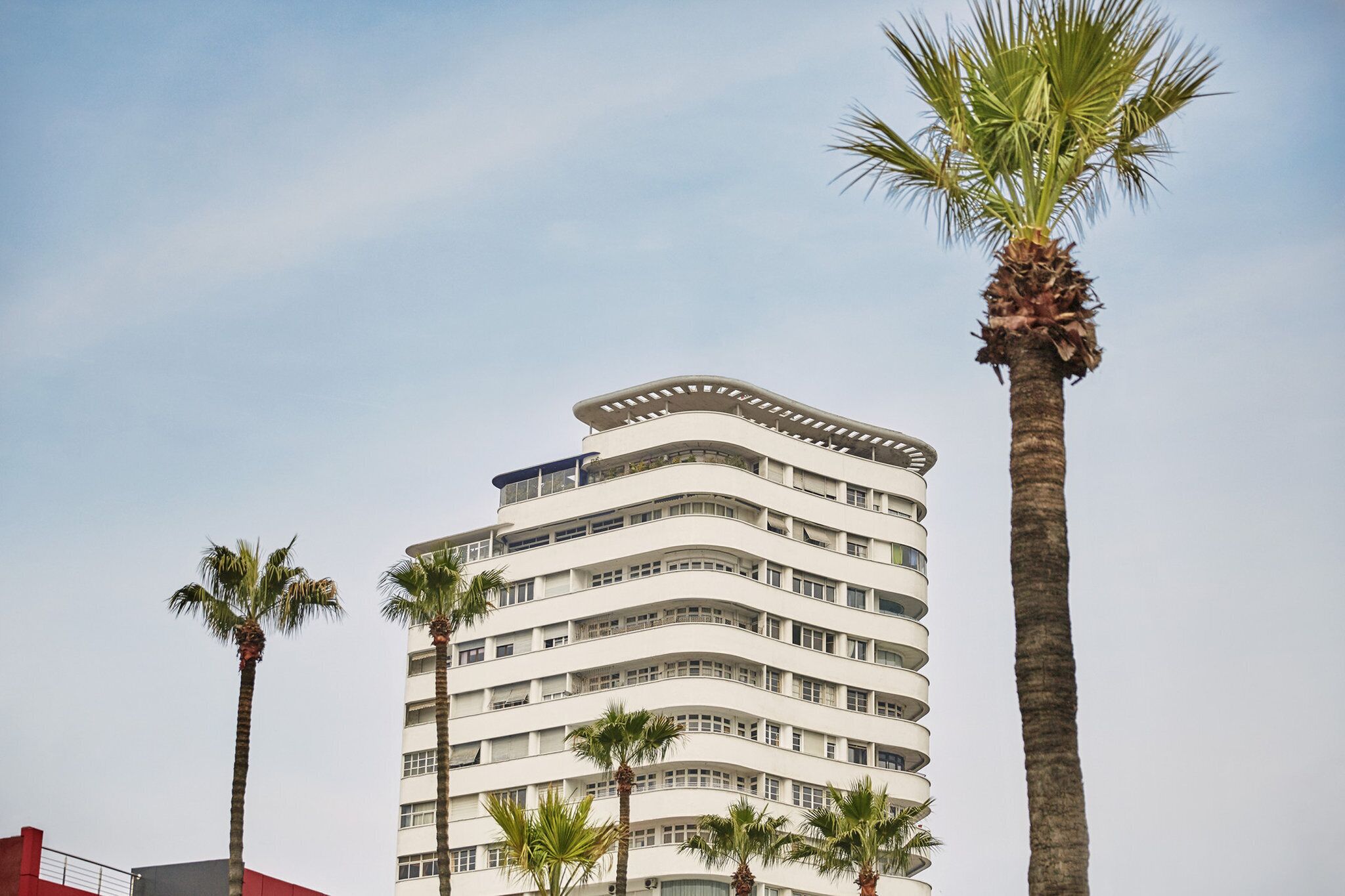 A multi-story building with a curved facade, surrounded by palm trees.