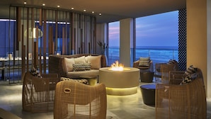 Un salón moderno con muebles de mimbre, una chimenea central y vistas al océano.