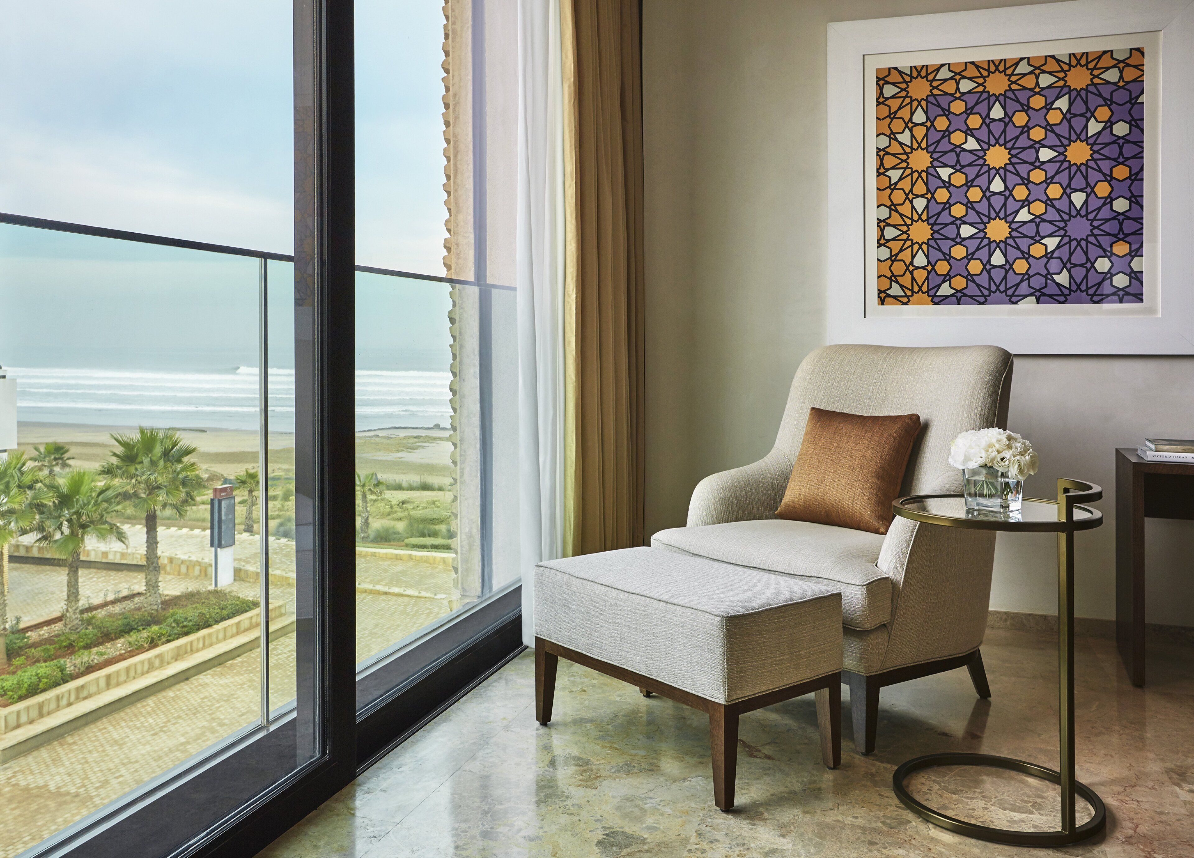 Una habitación moderna con vista a la playa, un sillón cómodo, una mesita auxiliar y una obra de arte enmarcada en la pared.