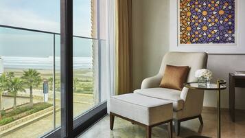 Une chambre moderne avec vue sur la plage, un fauteuil confortable, une petite table d’appoint et une œuvre d’art encadrée au mur.