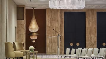 A conference room with a podium, rows of chairs, a large chandelier, and a decorative hanging light fixture.