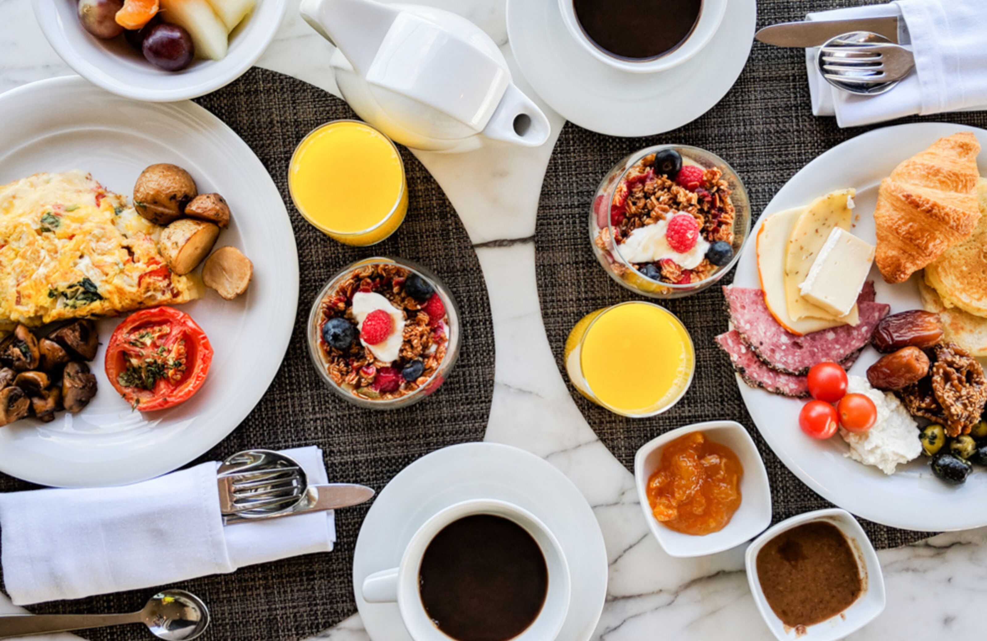 A breakfast setting with plates of food, including eggs, toast, and fruit, along with cups of coffee and juice.