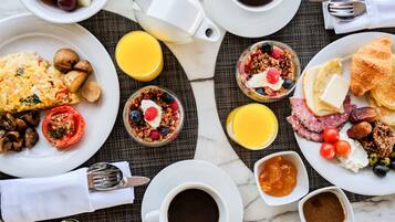 A breakfast setting with plates of food, including eggs, toast, and fruit, along with cups of coffee and juice.