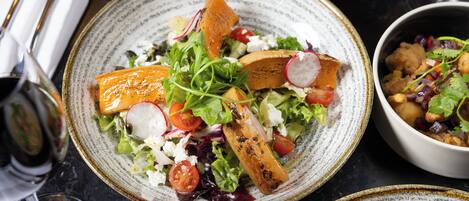 A dining table with a plate of salad, a bowl of chickpeas, and a wine glass.