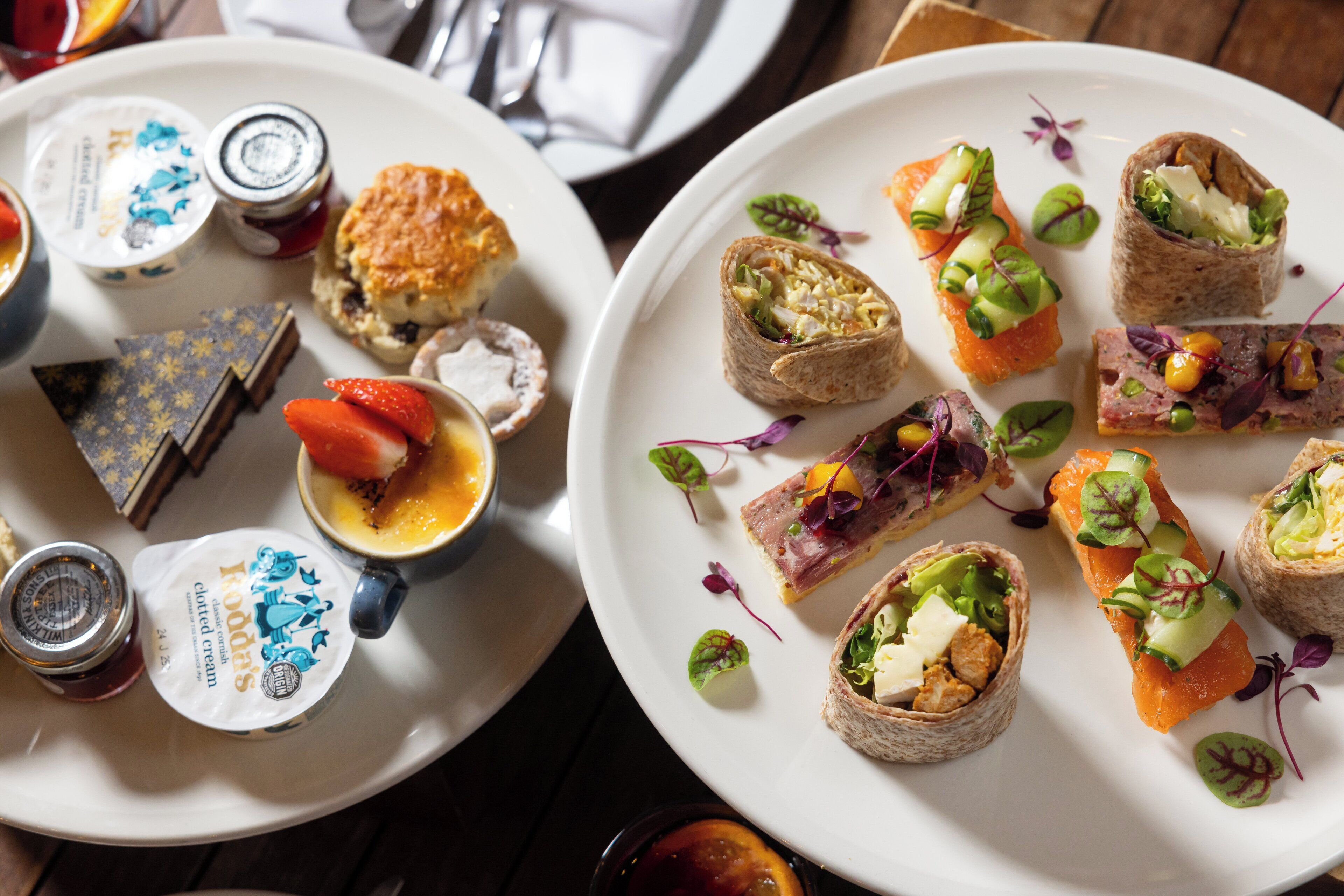 A variety of appetizers on white plates, including wraps, scones, and a small bowl of cream.