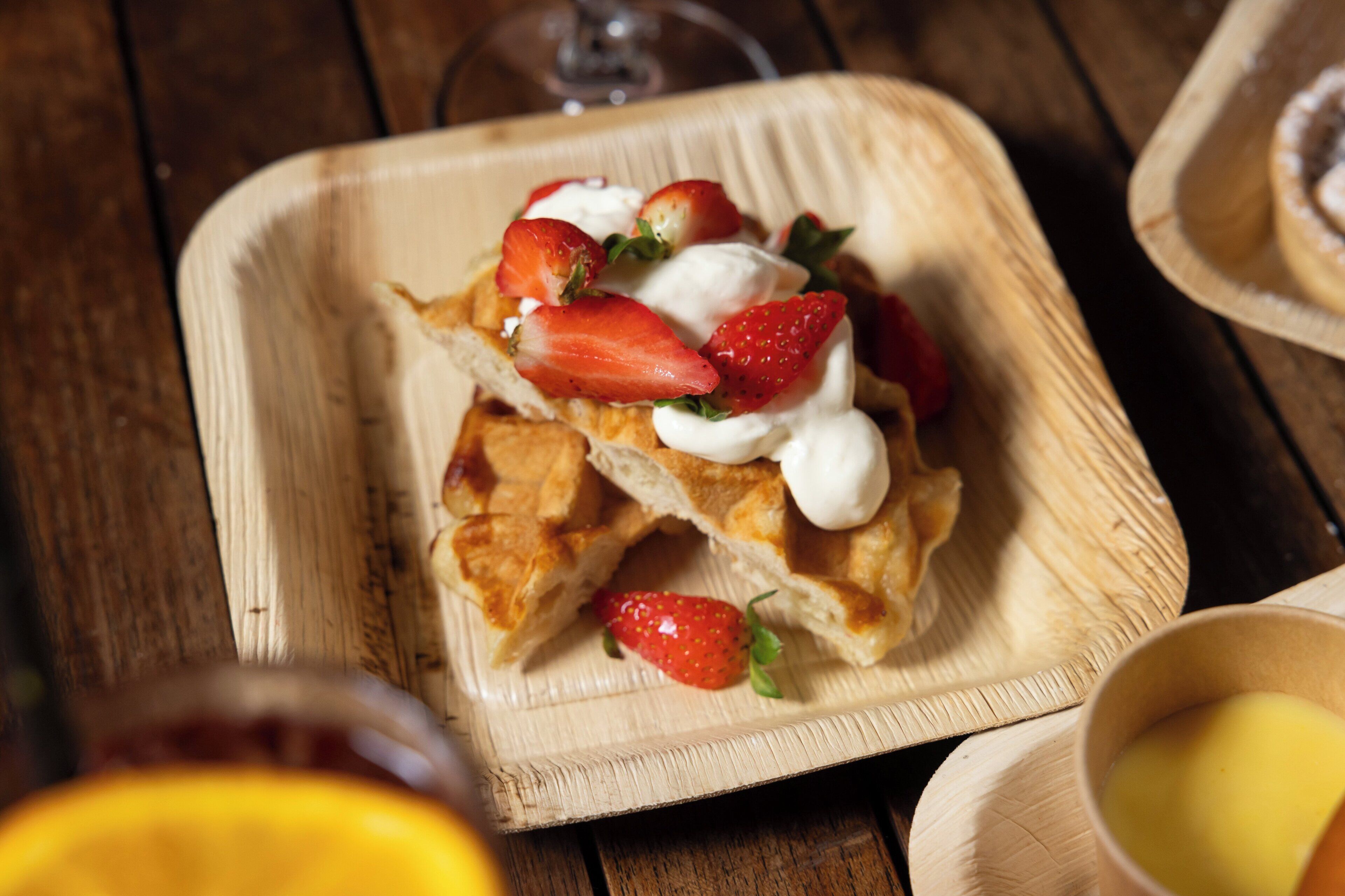 Une assiette carrée en bois sur laquelle est servi un dessert garni de fraises et de crème fouettée.