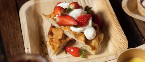 Un plato de madera cuadrado con un postre cubierto de fresas y crema batida.