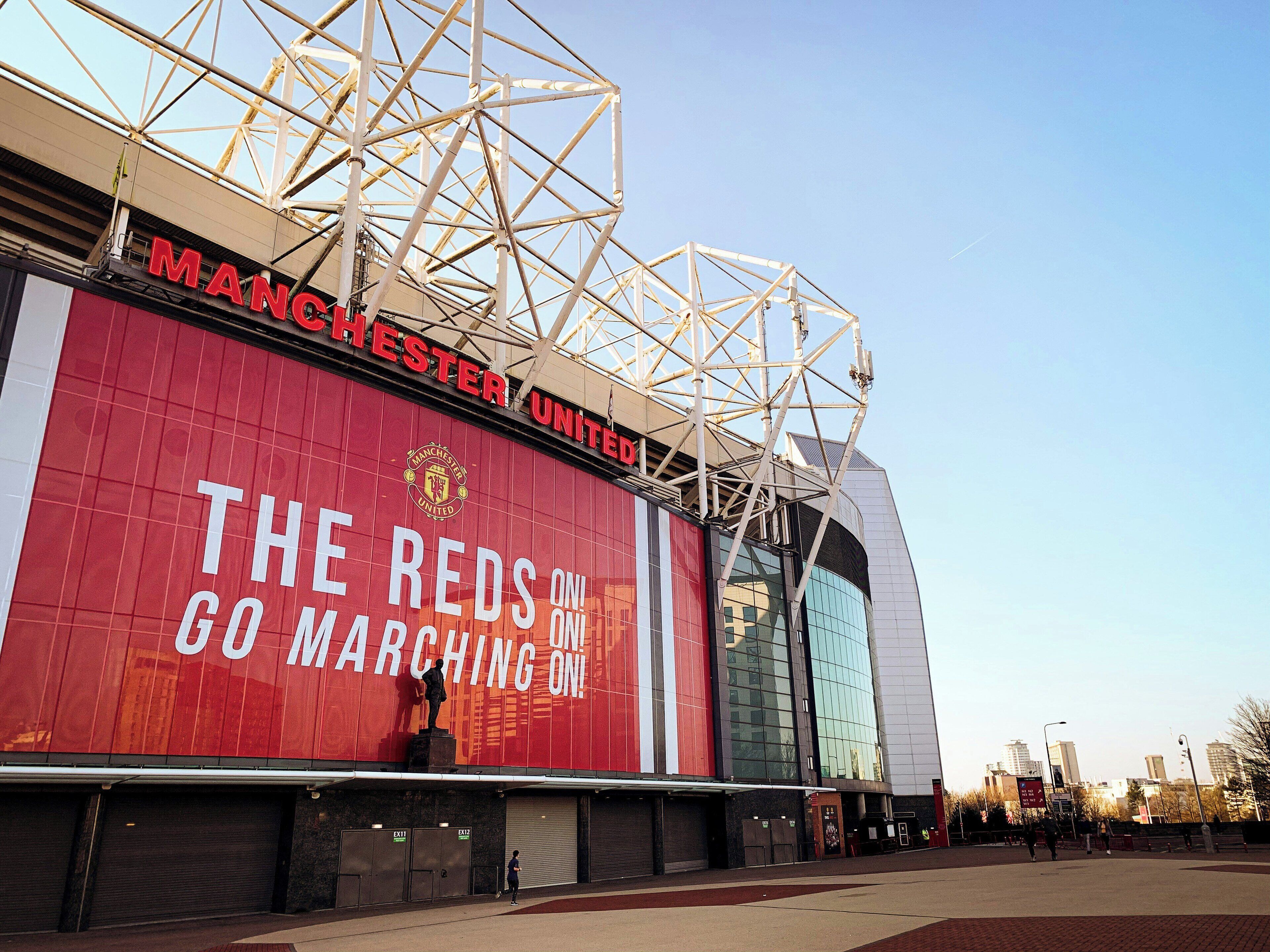Un estadio con un gran letrero rojo que dice 'Manchester United' y 'Los Reds Marchan Avante'.