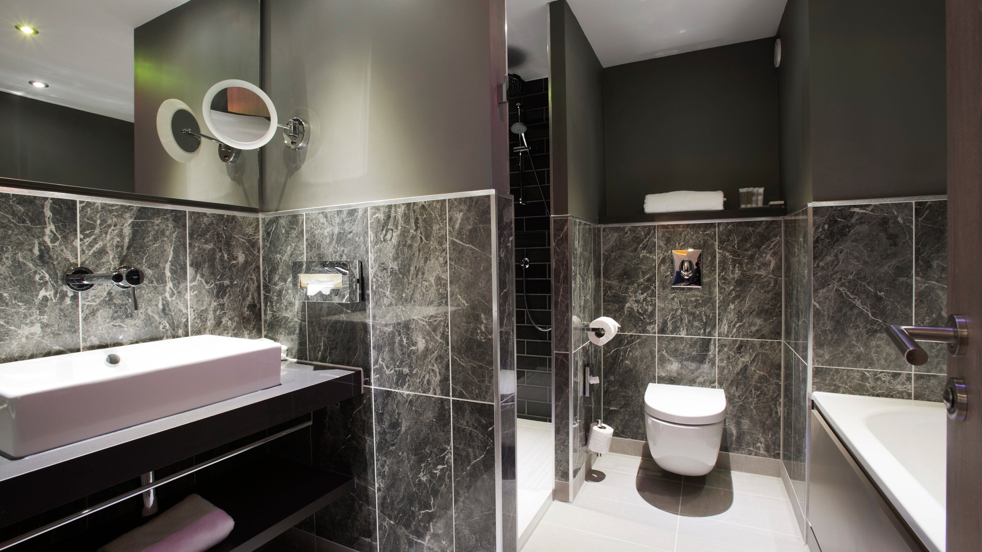 Ein modernes Badezimmer mit weißem Waschbecken, Spiegel und Toilette. Es verfügt über Marmorwände und eine Duschkabine aus Glas.