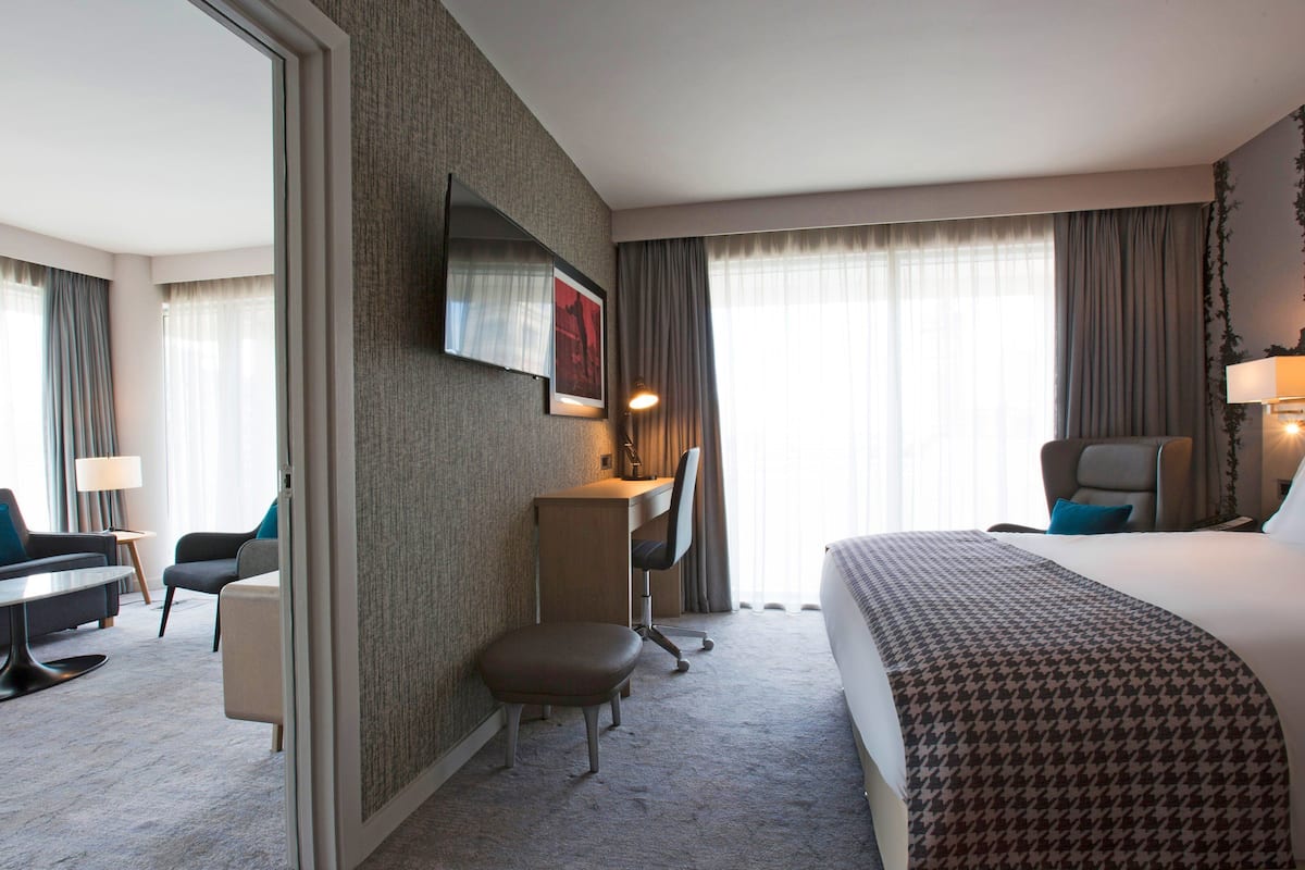 A hotel room with a bed, a desk, a chair, a sofa, and a TV.