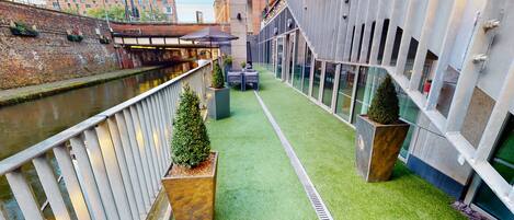 A narrow corridor with artificial grass, potted plants, and a view of a river.