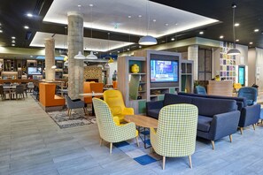 A modern lounge area with seating, a television, and a bookshelf. - Holiday Inn Manchester - City Centre by IHG (Manchester)