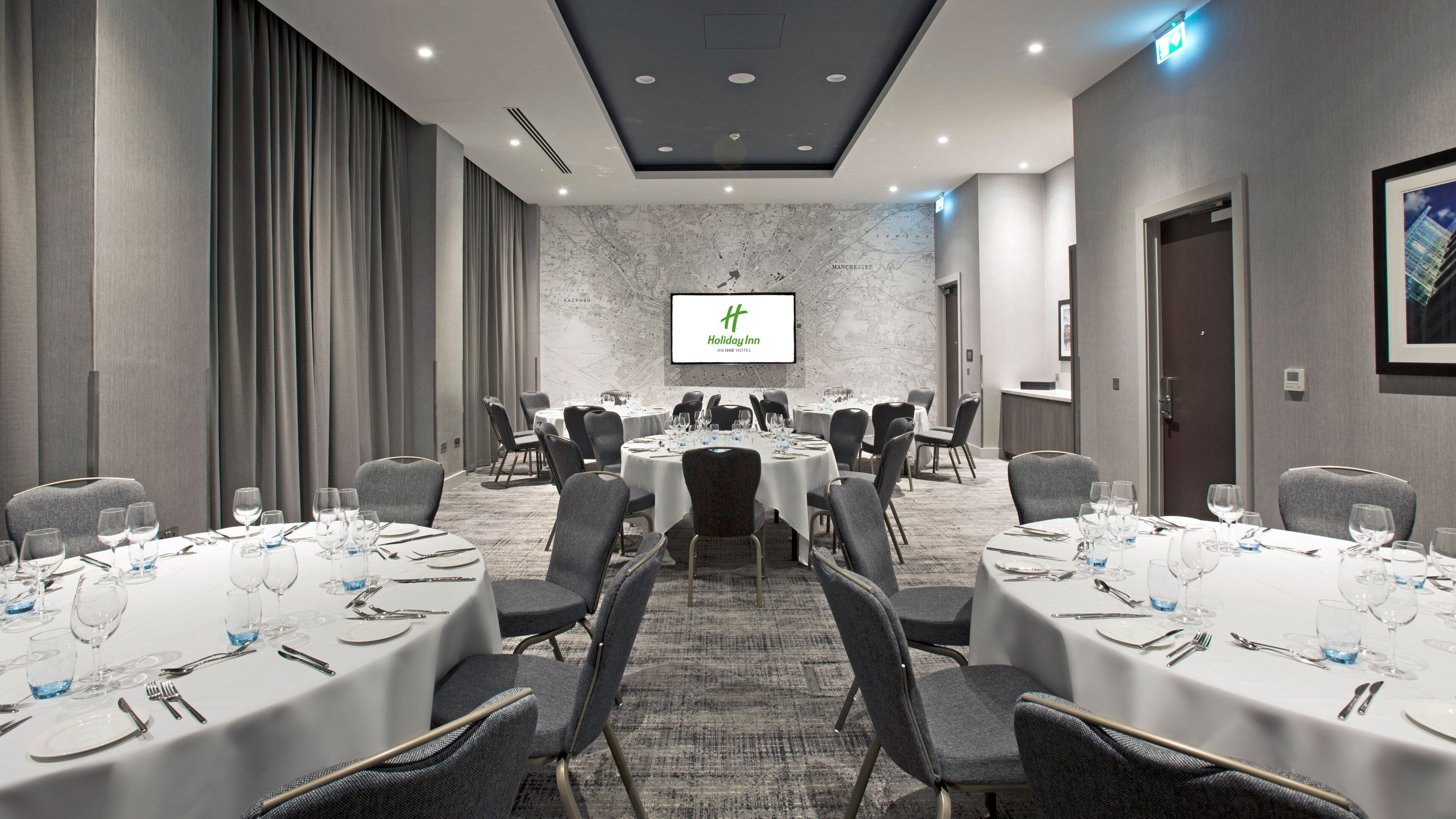 Una sala conferenze con tavoli rotondi, sedie e un grande schermo che mostra il logo Holiday Inn.