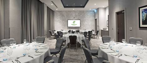A conference room with round tables, chairs, and a large screen displaying the Holiday Inn logo.