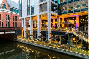 A riverside restaurant with outdoor seating, a staircase, and a canal. - Holiday Inn Manchester - City Centre by IHG (Manchester)
