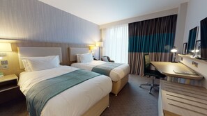 A hotel room with two beds, a desk, a chair, and a large window with curtains. - Holiday Inn Manchester - City Centre by IHG (Manchester)