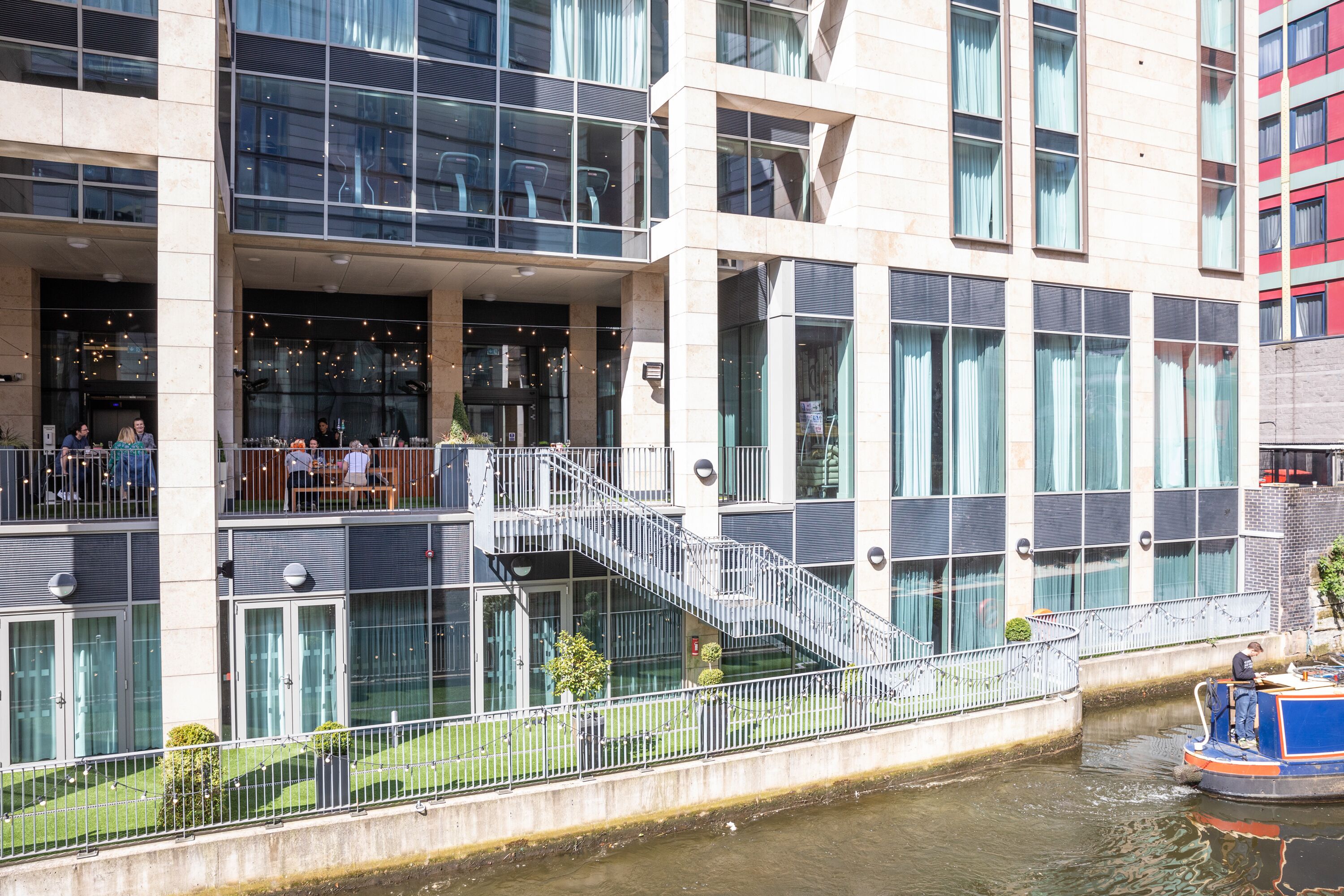 A modern building with a glass facade, a staircase leading to a balcony, and a canal with a boat.
