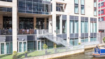 A modern building with a glass facade, a staircase leading to a balcony, and a canal with a boat.