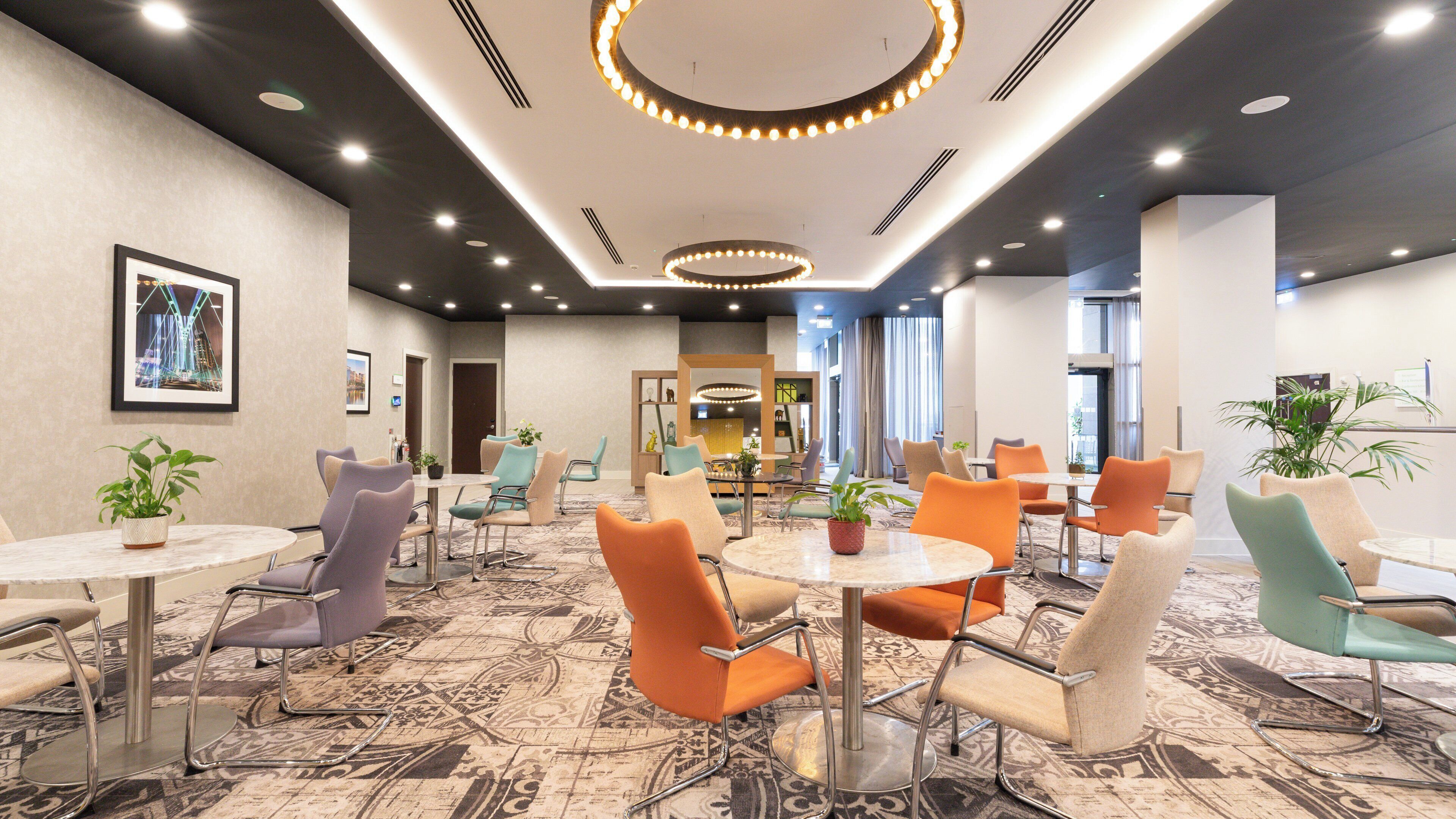 A hotel lobby with round tables, chairs, and a large mirror.