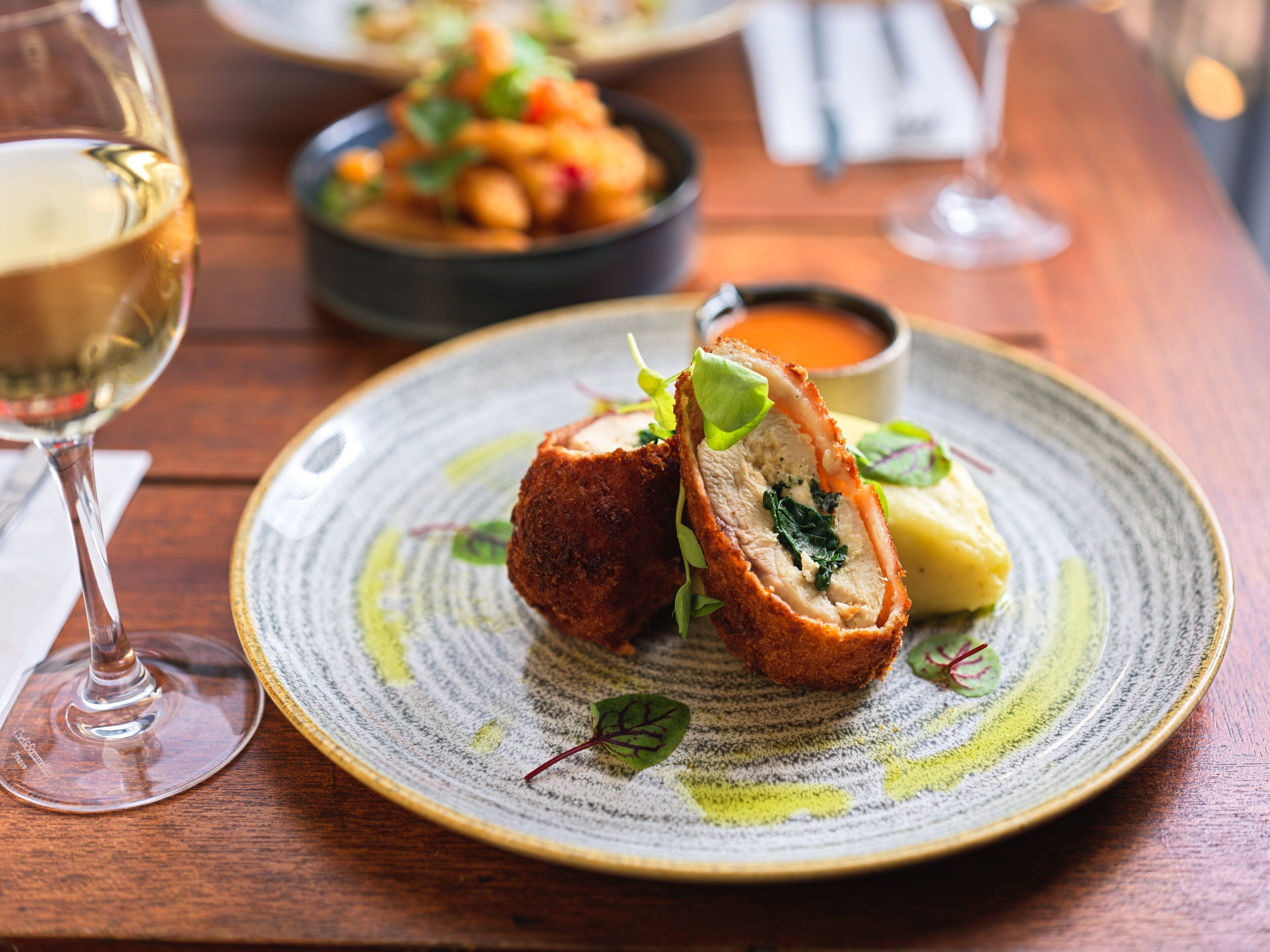 Une assiette de nourriture comprenant un plat de viande farci, un bol de soupe et un verre de vin blanc, le tout posé sur une table en bois.