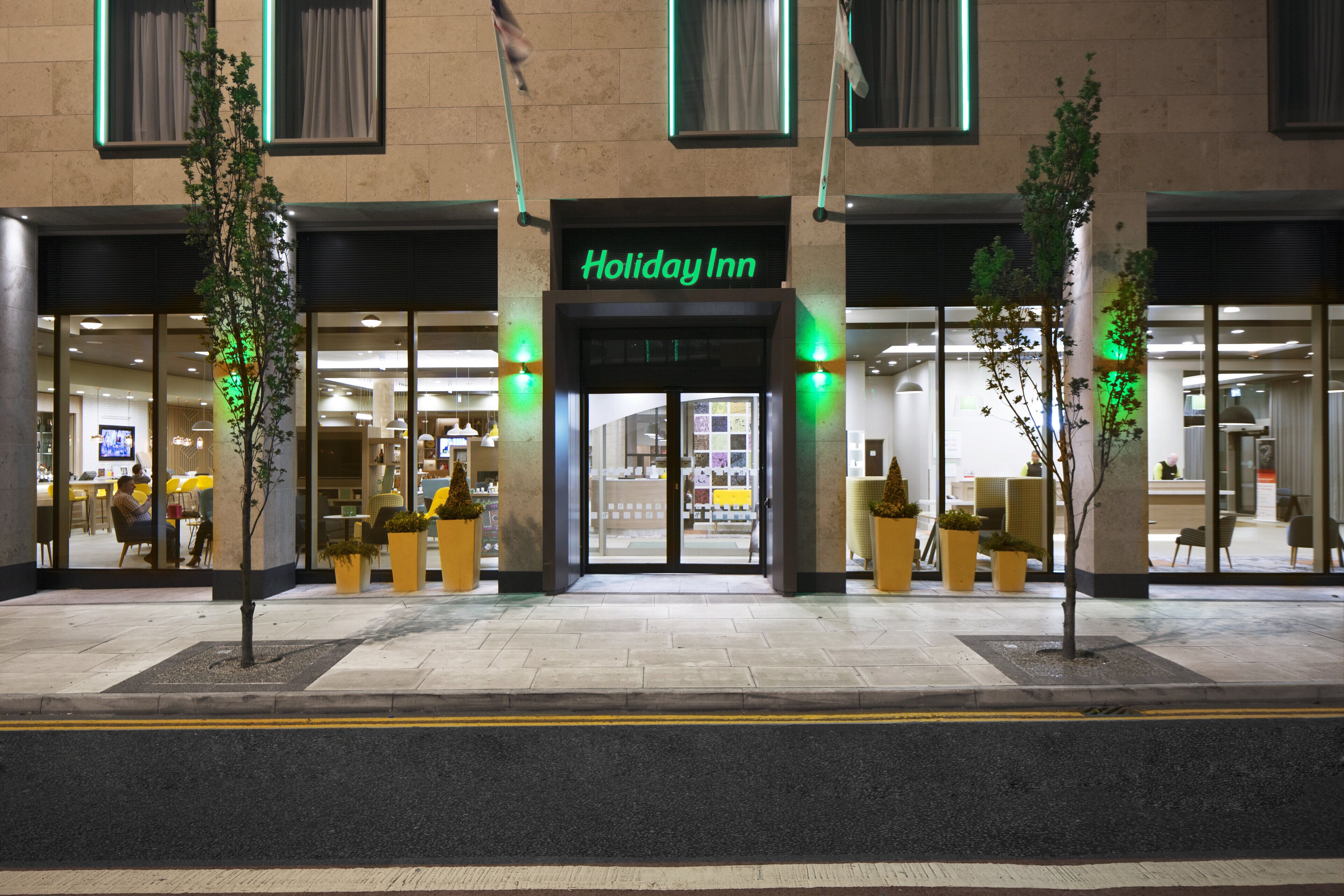 The exterior of a Holiday Inn hotel with a modern facade, large windows, and a prominent entrance.