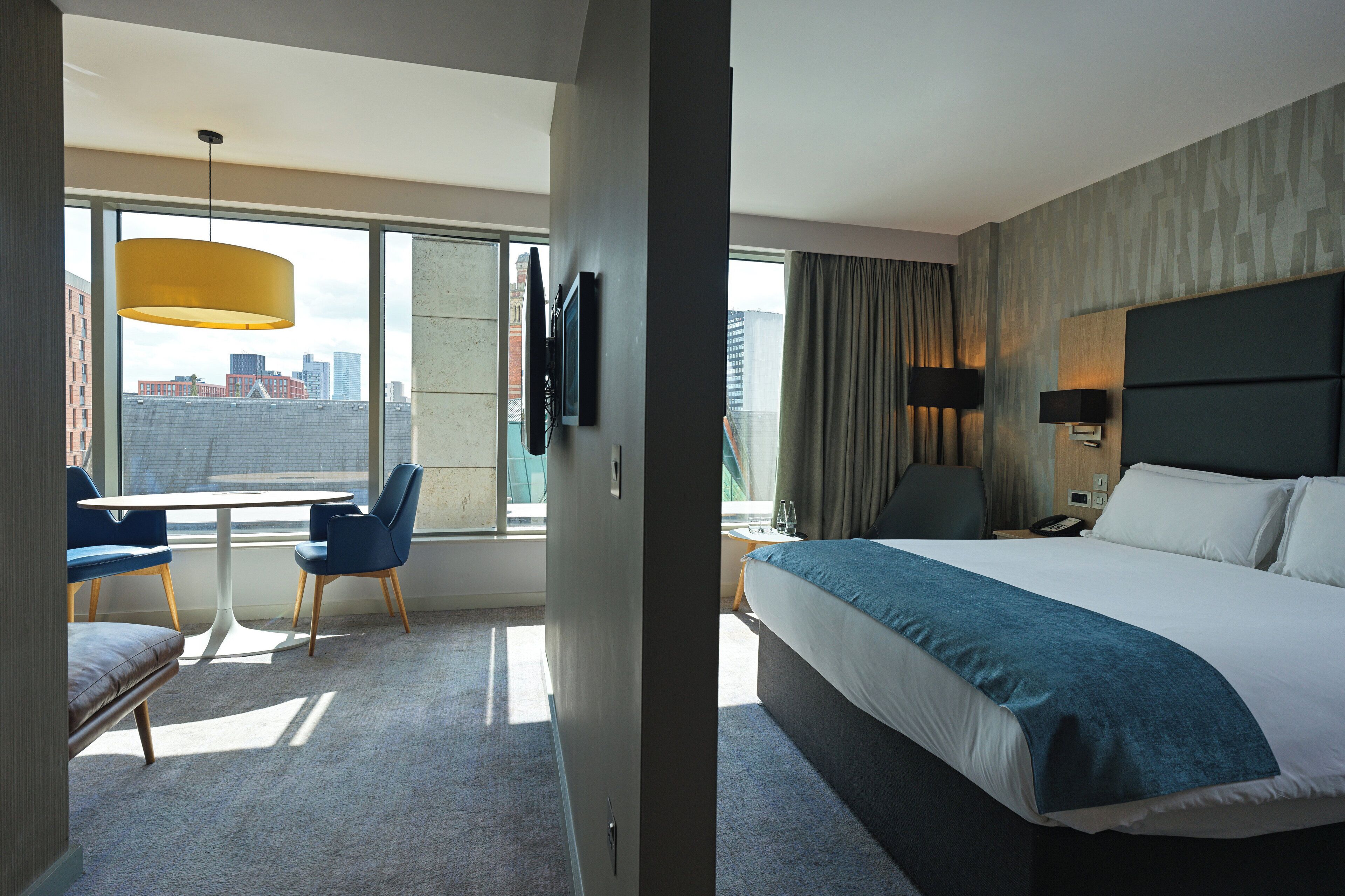 Een moderne hotelkamer met een groot bed, een bureau met stoelen, een televisie en uitzicht op de stad.